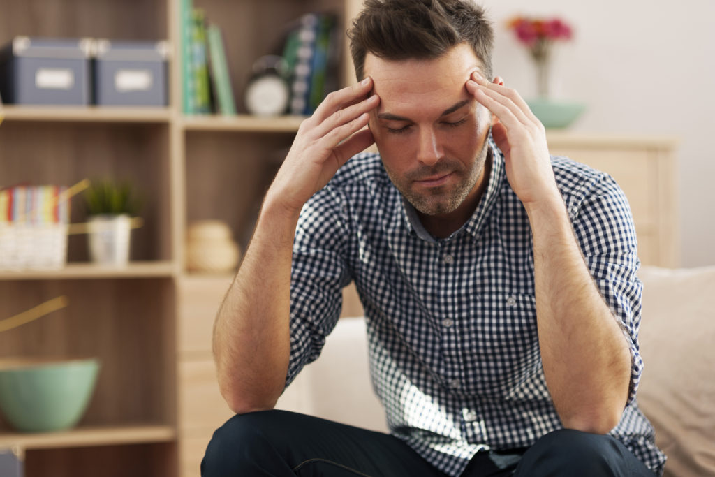 man sitting at home holding his head 