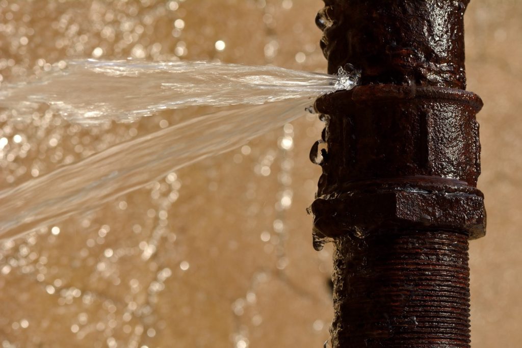 water bursting out of a pipe, calling for leak detection services