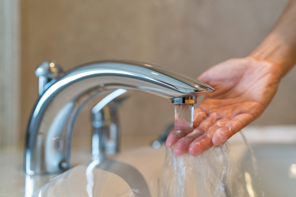 A person placing their hand under a sink faucet with running water
