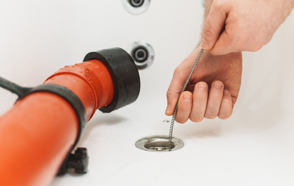 A plumber putting a tool down a drain next to an orange plumbing tool in El Paso.